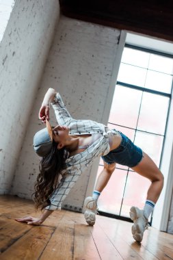 low angle view of beautiful dancer touching cap and dancing hip-hop in dance studio 