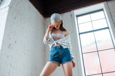 low angle view of dancer covering face with cap and posing in dance studio 