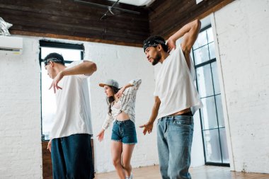 multicultural dancers in headbands and attractive girl in cap dancing hip-hop 