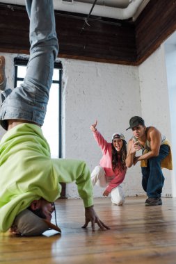 selective focus of emotional dancers looking at african american man breakdancing in dance studio 