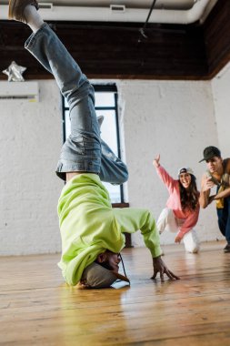 selective focus of african american man in cap breakdancing near emotional dancers 