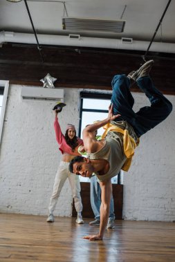 selective focus of man breakdancing near excited multicultural dancers 