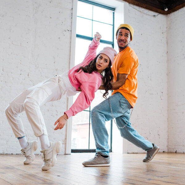 interracial couple in hats breakdancing in dance studio 