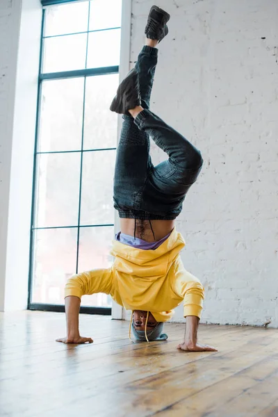 stylish man in hat doing handstand while breakdancing in dance studio