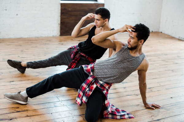 handsome multicultural dancers touching hair while dancing in dance studio 