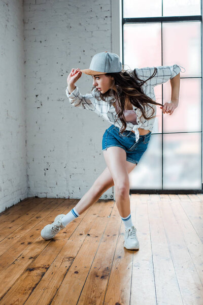 young woman in denim shorts touching cap and dancing hip-hop 