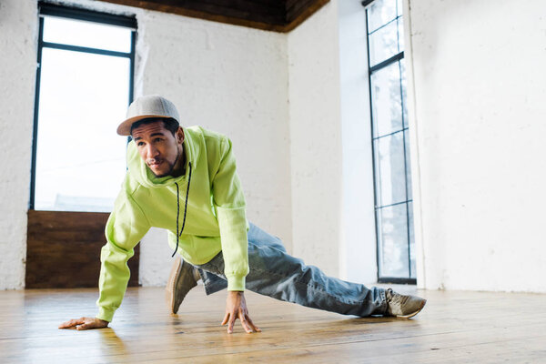 handsome african american man in cap breakdancing in dance studio 