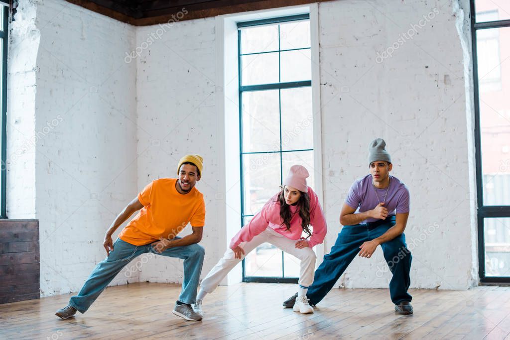 stylish multicultural men and girl in hats breakdancing