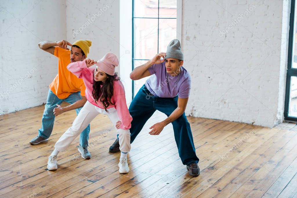 young multicultural dancers touching hats while breakdancing