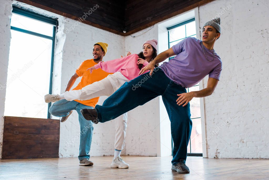 stylish multicultural men in hats breakdancing with beautiful woman 
