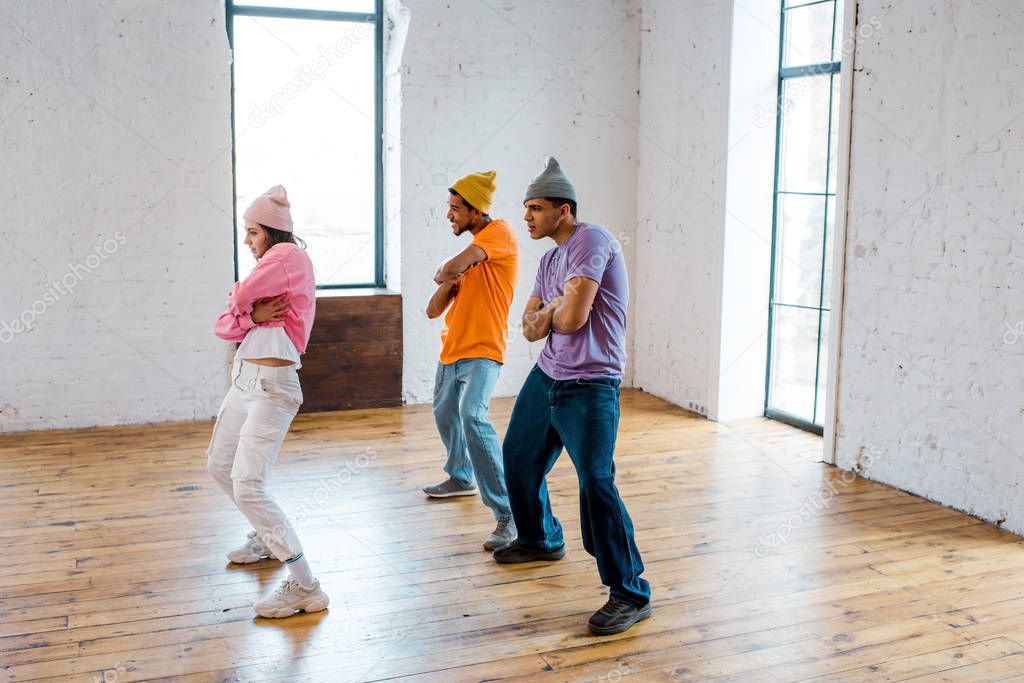 stylish girl with crossed arms breakdancing with handsome multicultural men in hats 