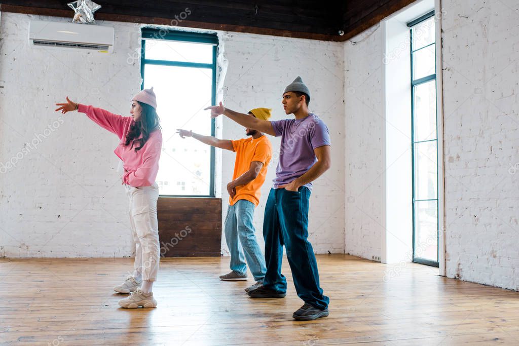 side view of attractive girl gesturing while breakdancing with handsome multicultural men in hats 