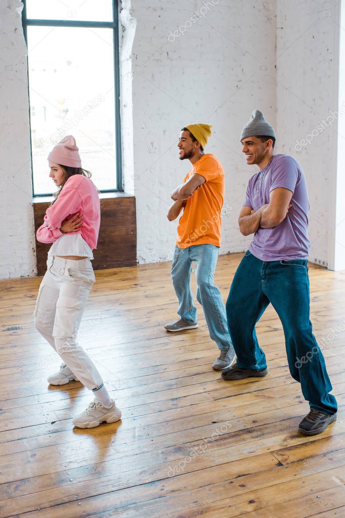 attractive girl with crossed arms breakdancing with stylish multicultural men in hats 