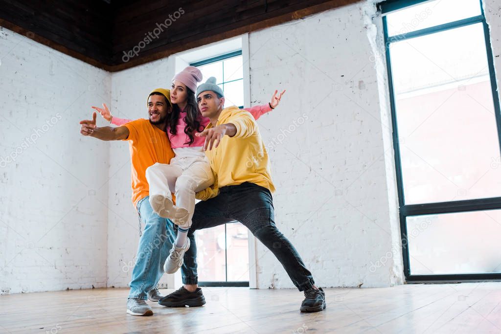 multicultural men in hats holding attractive dancer 