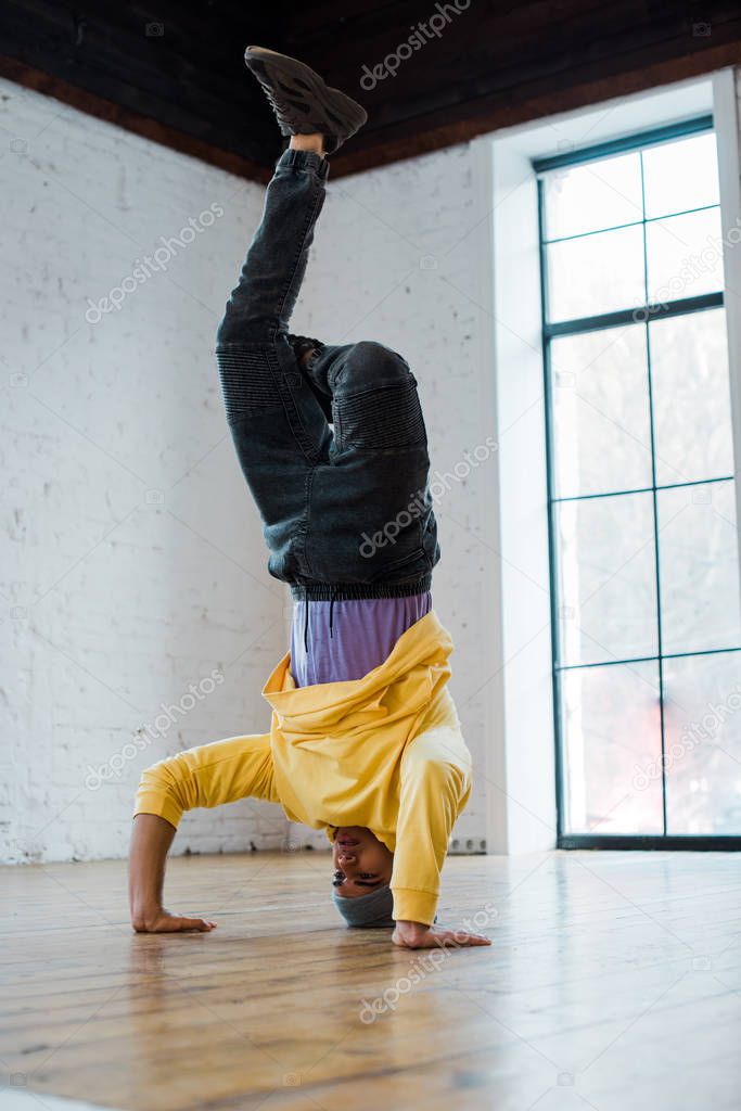 man in hat breakdancing and doing handstand in dance studio 