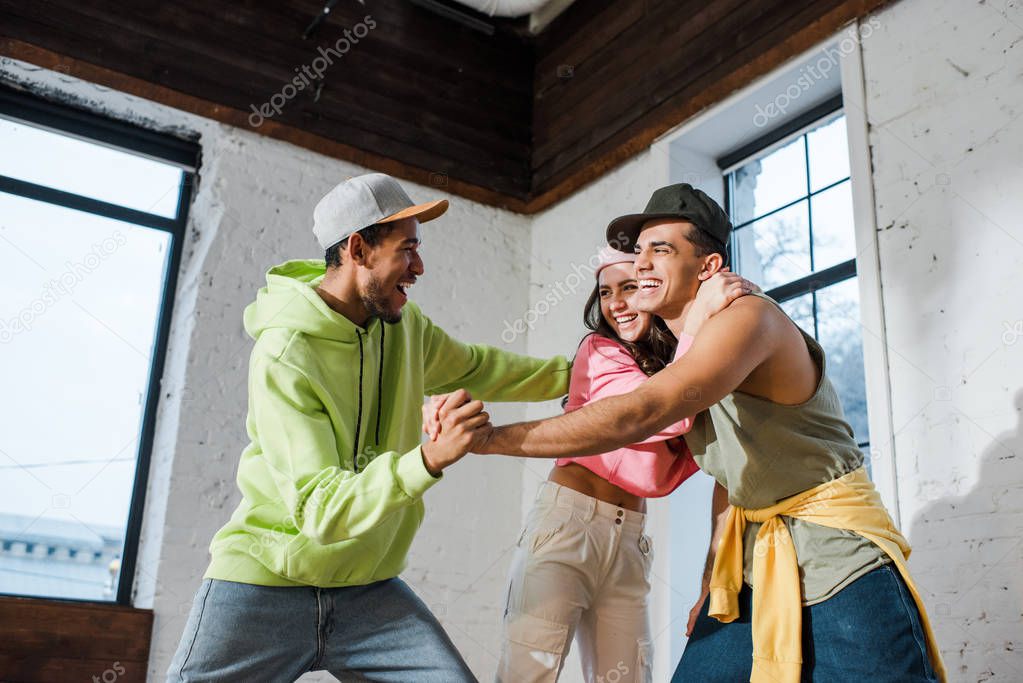 excited multicultural dancers holding hands near happy woman 