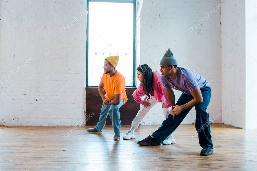young woman and stylish multicultural men stretching in dance studio 