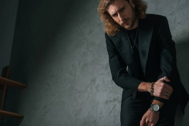 Gri duvarın yanında siyah takım elbiseli, gergin moda işadamının düşük açılı görüntüsü