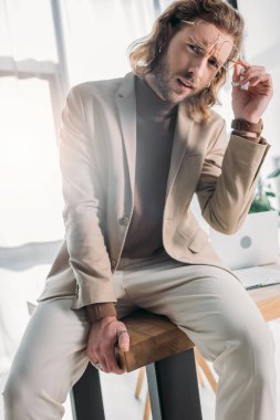 Masada oturan şık moda işadamının düşük açılı görüntüsü ve ofisteki kameraya bakıyor.