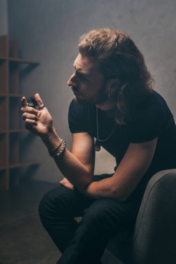 Gri duvarın yanındaki koltukta oturan siyah elbiseli şık iş adamı.