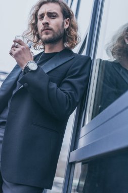 Siyah takım elbiseli şık bir işadamının elinde ofis binasının yakınında viski bardağı tutarken düşük açılı görüntüsü.