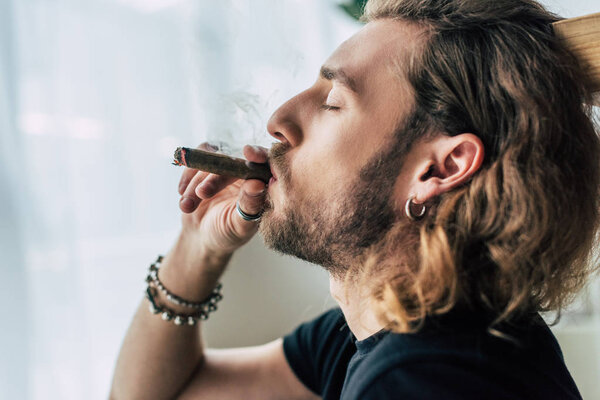 side view of fashionable casual businessman in total black outfit smoking cigar with closed eyes in office