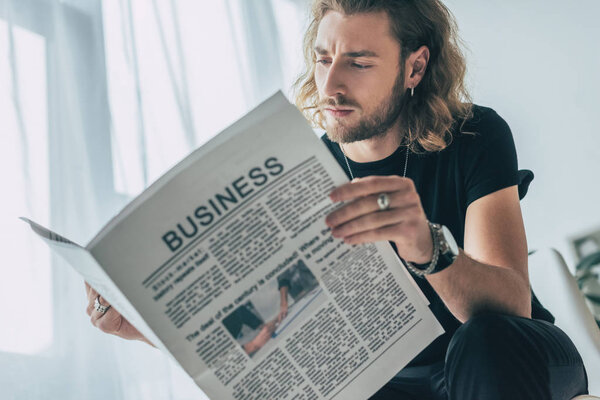 fashionable casual businessman in total black outfit reading business newspaper in office