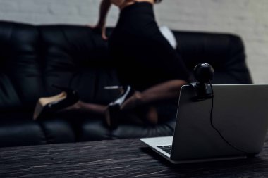 Dizüstü bilgisayardaki web kamerasının seçici odak noktası çoraplı seksi kız ve koltukta yüksek topuklu ayakkabılar, kırpılmış manzara.