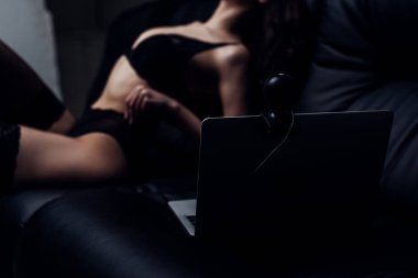 Seçici odak noktası siyah iç çamaşırlı seksi kız diz üstü bilgisayarda poz veriyor ve kanepenin üzerinde kamera var.