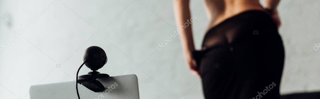 Panoramic shot of sexy girl taking off skirt in front on laptop with web camera, selective focus