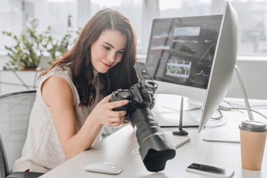Mutlu sanat editörü dijital kamerayı bilgisayar monitörlerinin yanında tutuyor 
