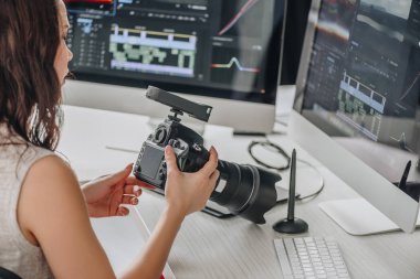 art editor holding digital camera near table with computer monitors  clipart