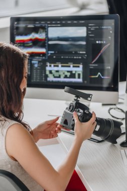 editor holding digital camera near table with computer monitors  clipart