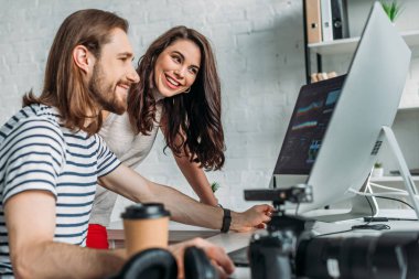 selective focus of happy art editor looking at computer monitor near coworker  clipart