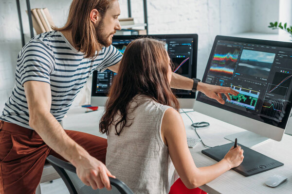 Художественный редактор показывает пальцем на монитор компьютера рядом с женщиной
 