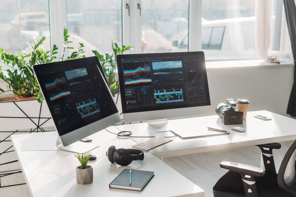 мониторы с раскадровкой рядом с наушниками и бумажной чашкой на столе
 