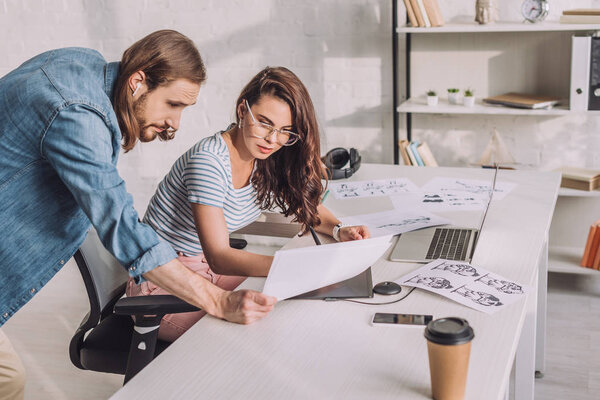 illustrator holding sketch near coworker in glasses 