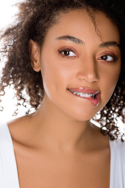 happy african american girl with dental braces biting lip, isolated on white