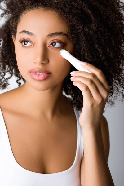 beautiful african american girl using eye roller, isolated on grey