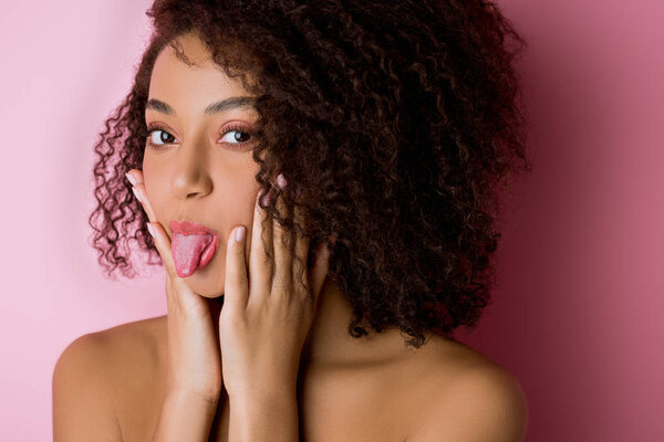 portrait of funny african american girl sticking tongue out on pink
