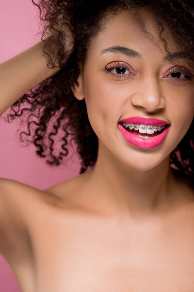счастливый положительный голый африканский американец девушка с зубными скобками, изолированные на розовый
