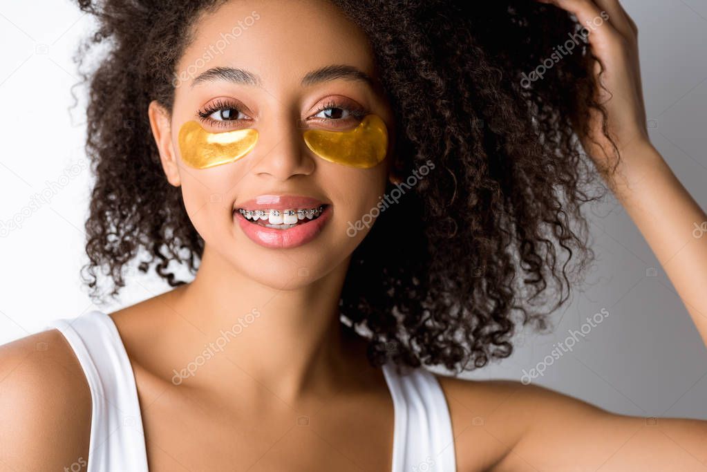 attractive smiling african american girl with golden eye patches and dental braces, isolated on grey