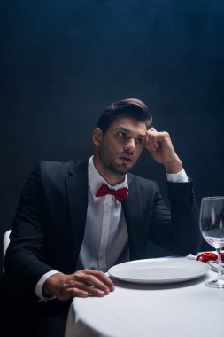 Handsome man in suit looking away at served table isolated on black clipart