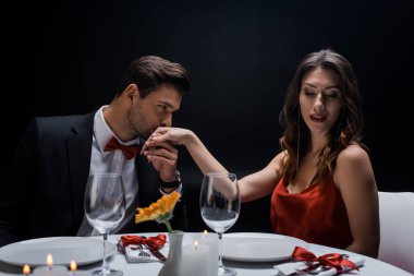 Siyahlar içinde izole edilmiş romantik bir akşam yemeğinde zarif bir erkek, çekici bir kadının elini öpüyor.