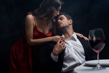 Seçici odak noktası, siyah üzerine izole edilmiş romantik bir akşam yemeği sırasında erkek arkadaşının düğmelerini açan güzel kadın.