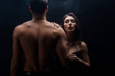 Seksi kadın kaslı erkek arkadaşının yanında duruyor ve siyah kameraya bakıyor.