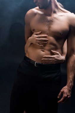 Siyah arka planda kaslı adama dumanla sarılan kadın görüntüsü.