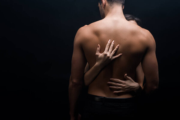 Woman touching back of shirtless man isolated on black
