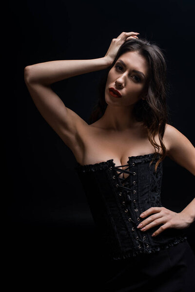 Sexy woman in black corset looking at camera isolated on black