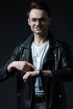 Gülümseyen stil sahibi, motorcu ceketli, siyah üzerine izole edilmiş kol saatini gösteren vahşi adam.